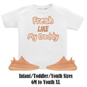 May include: White t-shirt with the text "Fresh Like My Daddy" in peach-coloured letters. The shirt is paired with a pair of peach-coloured trainers. Infant/Toddler/Youth sizes 6M to Youth XL.