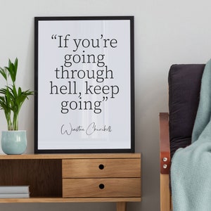 Könnte beinhalten: Ein gerahmter Druck mit dem Zitat "If you're going through hell, keep going" von Winston Churchill. Der schwarze Rahmen umgibt einen weißen Hintergrund mit schwarzem Text. Der Druck befindet sich auf einem Holzschrank mit einer kleinen Pflanze in einem blauen Topf.