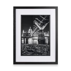 May include: A black and white photograph of the Millennium Bridge in London at night. The bridge is illuminated and the iconic St Paul's Cathedral can be seen in the background.
