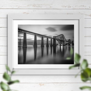 May include: A black and white photograph of a bridge over a body of water. The bridge is made of metal and has a series of arches. The water is calm and reflects the bridge.