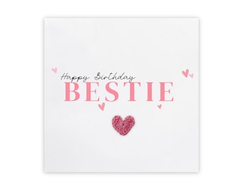 Puede incluir: Una tarjeta blanca con corazones rosas y el texto "Happy Birthday BESTIE" en letras rosas. Un corazón rosa de ganchillo está en el centro de la tarjeta.