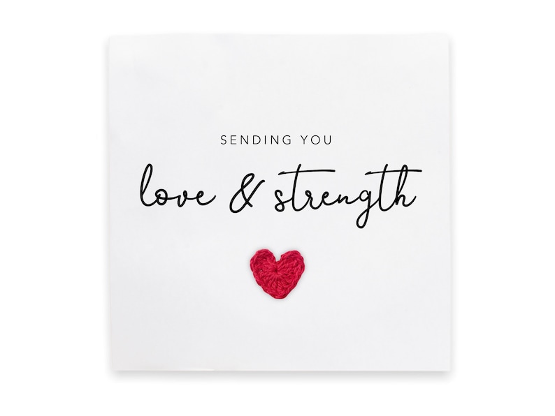 May include: A white card with the text "Sending you love & strength" in black cursive font. A small red crocheted heart is below the text.