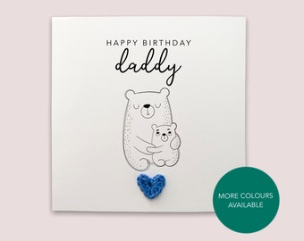 Op de afbeelding: Een witte kaart met de tekst "Happy Birthday Daddy" en een zwart-witte illustratie van twee beren die elkaar knuffelen. Een blauw gehaakt hart is aan de kaart bevestigd. De tekst "Meer kleuren beschikbaar" is gedrukt op een groene cirkel.