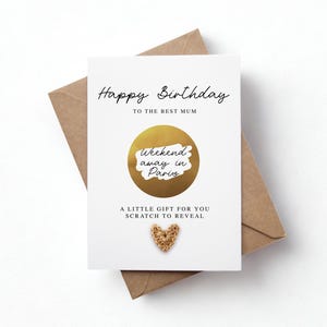 Könnte beinhalten: Eine weiße Geburtstagskarte mit dem Text "Happy Birthday To The Best Mum" in schwarzer Schrift. Sie zeigt einen goldenen Rubbelkreis mit "weekend away in Paris" und ein kleines goldenes Herz. Die Karte liegt auf einem braunen Umschlag.