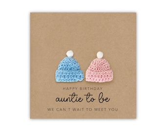 May include: A brown card with the text "Happy Birthday auntie to be We can't wait to meet you". Two small crocheted hats, one blue and one pink, are placed above the text.