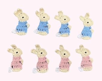 May include: Eight crocheted bunny rabbit embellishments. Four are light blue and four are light pink. Each bunny has a cream colored body and a white tail.