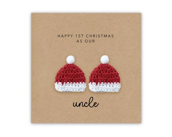 May include: A Christmas card with a brown background and two small red and white crocheted Santa hats with white pom-poms. The text "Happy 1st Christmas as our uncle" is printed below the hats.