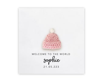 May include: A white card with a pink crocheted hat with a white pom-pom on top. The card says "Welcome to the world Sophie 21.05.223"