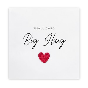 Può includere: Un biglietto di auguri bianco con le parole "Big Hug" in elegante scrittura. Un piccolo cuore rosso all'uncinetto è centrato sotto il testo. Le parole "Small Card" sono sopra il testo principale.