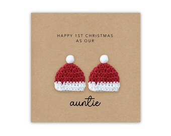 May include: A brown card with the text "Happy 1st Christmas as our auntie" and two small red and white crocheted Santa hats.