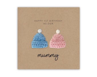 May include: Happy 1st Birthday as our Mummy card with two crocheted hats, one blue and one pink, with white pom-poms on top.