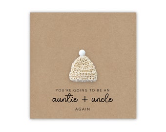 May include: A brown card with a small white crocheted hat with a white pom-pom on top. The card says "You're going to be an auntie + uncle again."