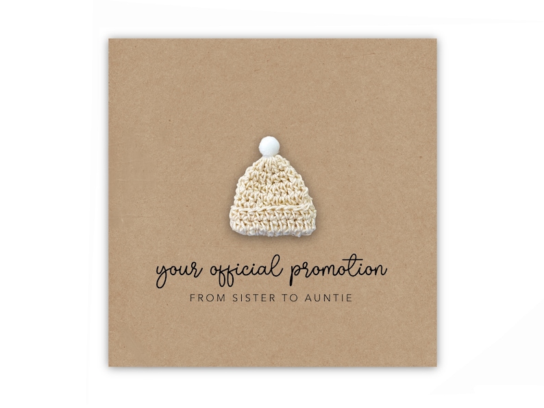 May include: A card with a brown background and a small white knitted hat with a white pom-pom on top. The text on the card reads "your official promotion from sister to auntie".