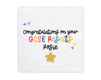 May include: A white card with the text "Congratulations on your GCSE Results Rosie" in black script. The words "GCSE Results" are in rainbow colors. There are small pink and blue hearts and a gold star on the card.