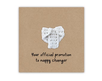 May include: A brown card with a white crocheted diaper on it. The card says "Your official promotion to nappy changer".