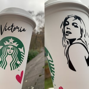 May include: A white reusable coffee cup with a green Starbucks logo, the name "Victoria" written in black script, and a pink heart. The second cup is white with a black silhouette of a woman's face.