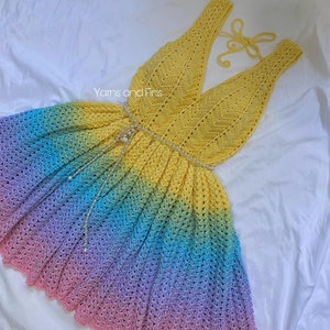 May include: A rainbow ombre crochet dress with a yellow crocheted bodice and a pearl beaded belt. "Yarns and Fins" is written on the dress.
