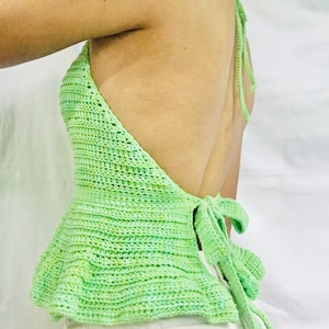Puede incluir: Un top de crochet verde con tirantes y lazada en la espalda. El top está hecho con hilo verde claro y verde oscuro.