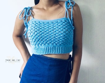 May include: A light blue crochet crop top with a criss-cross stitch pattern and thin straps. The top is worn over a dark blue skirt.