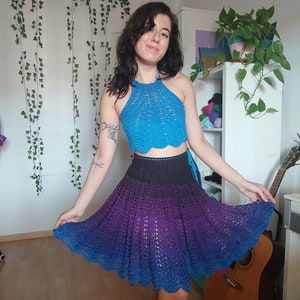 May include: A woman wearing a blue crochet halter top and a purple and blue ombre crochet skirt. The skirt is a-line and has a scalloped hem.