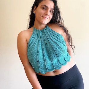 Op de afbeelding: Een turquoise haltertop met geschulpte rand. De top is gemaakt van gehaakt materiaal. Het model draagt een zwarte legging. Een uniek en stijlvol kledingstuk.
