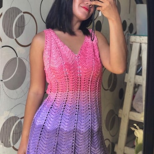 May include: A sleeveless crochet dress with a pink to purple ombre colour gradient. The dress has a V-neck and a loose fit.