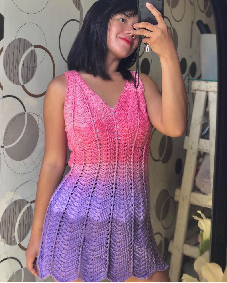 May include: A sleeveless crochet dress with a pink to purple ombre colour gradient. The dress has a V-neck and a loose fit.