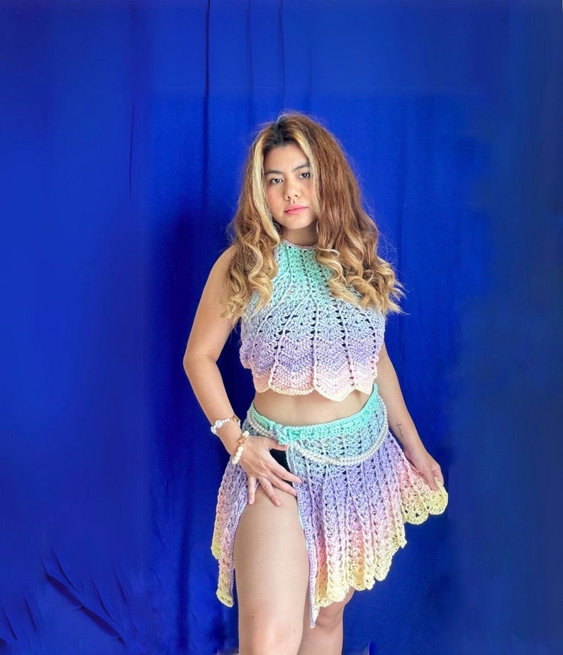 May include: A woman wearing a rainbow ombre crochet top and skirt. The top is a halter style and the skirt is a wrap style with a slit up the side.