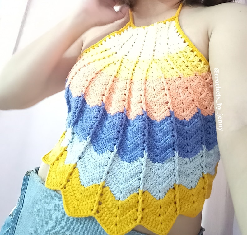 Op de afbeelding: Een handgemaakte, veelkleurige gehaakte haltertop. De top heeft een chevronpatroon in tinten geel, perzik, blauw en wit. De top is een zomerkledingstuk, perfect voor warm weer. De top is een uniek, handgemaakt stuk.