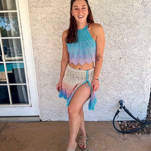 May include: A woman wearing a light blue and pink crochet halter top and matching skirt. The skirt has a side slit and is tied at the waist. She is wearing sandals with rhinestones.