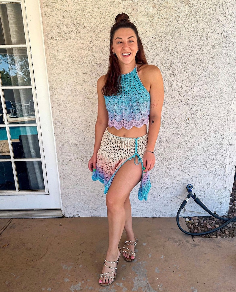 May include: A woman wearing a light blue and pink crochet halter top and matching skirt. The skirt has a side slit and is tied at the waist. She is wearing sandals with rhinestones.