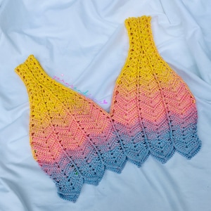 May include: A crocheted top with a gradient of yellow, pink and blue. The top has a V-neck and a scalloped hem.