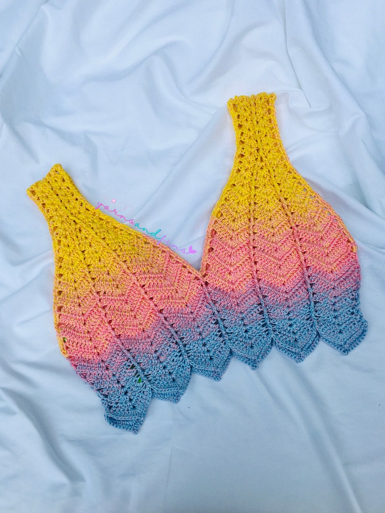 May include: A crocheted top with a gradient of yellow, pink and blue. The top has a V-neck and a scalloped hem.