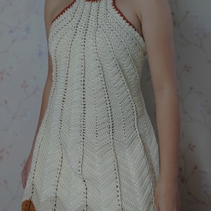 May include: A white crochet halter dress with a brown crocheted trim. The dress has a fitted bodice and a flared skirt.