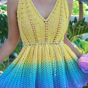 May include: A yellow, blue and purple crochet top with a white beaded belt. The top has a V-neck and a flared skirt.