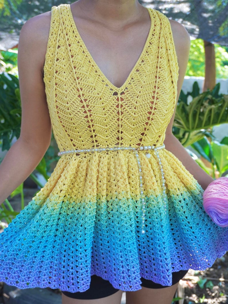 May include: A yellow, blue and purple crochet top with a white beaded belt. The top has a V-neck and a flared skirt.