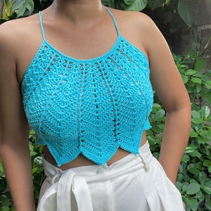 以下が含まれることがあります： 白のパンツの上に着た、薄いブルーのクロシェのホルターネックトップ。トップは、フリルのあるヘムラインです。