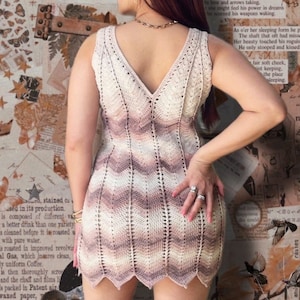 May include: A sleeveless crochet mini dress with a V-neckline. The dress is made of a soft, lightweight yarn and features a gradient colour pattern in shades of brown, beige, and white.