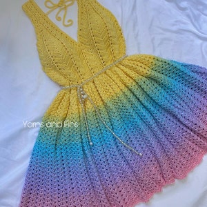 May include: A yellow, blue, green, and pink ombre crochet dress with a V-neck and a tie at the back. The dress has a beaded belt and is made with a delicate crochet stitch.