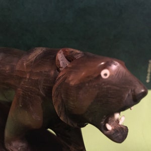 May include: A wooden carving of a bear with a snarling expression. The bear is brown and has white teeth and eyes. The carving is on a wooden base.
