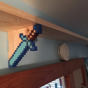 May include: A wooden shelf with two Minecraft sword brackets painted in blue, brown, and light blue. The shelf is mounted on a wall with a smoke detector.