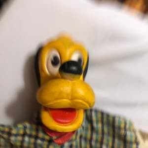 May include: A yellow and black puppet of a dog wearing a plaid shirt. The puppet has a large, open mouth with a red tongue.