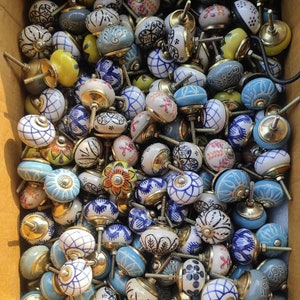 May include: A selection of ceramic cabinet knobs in a variety of colours and patterns. The knobs feature designs in blue, white, yellow, and red, with brass fittings. The assortment includes floral, geometric, and abstract motifs.