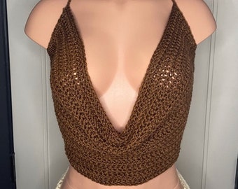 Puede incluir: Un top de ganchillo marrón con un diseño de cuello en V profundo. El top presenta finas correas y un patrón de tejido abierto texturizado. La prenda se exhibe en un maniquí.