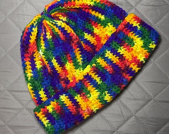 May include: A handmade, colorful crochet beanie hat. The hat features a vibrant rainbow pattern with red, orange, yellow, green, blue, and purple stripes. The brim is folded up, and the hat is made of soft yarn.