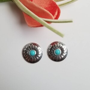May include: A pair of silver earrings with a turquoise stone in the center of each earring. The earrings have a floral design around the stone.