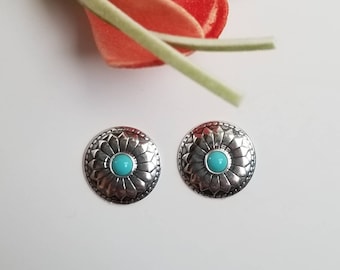 May include: A pair of silver earrings with a turquoise stone in the center of each earring. The earrings have a floral design around the stone.