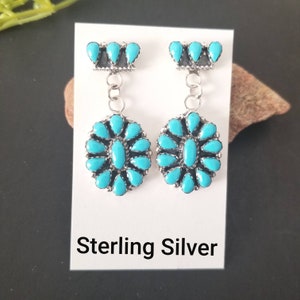 May include: Sterling silver earrings with turquoise stones. The earrings feature a cluster of turquoise stones in the shape of a flower, with a smaller cluster of turquoise stones at the top.