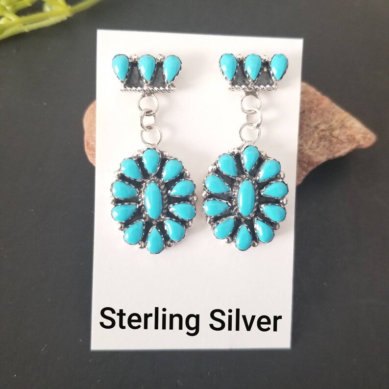 May include: Sterling silver earrings with turquoise stones. The earrings feature a cluster of turquoise stones in the shape of a flower, with a smaller cluster of turquoise stones at the top.