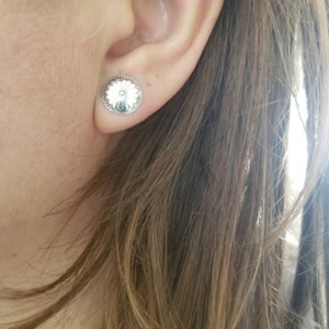 May include: A pair of silver stud earrings with a floral design. The earrings are round and have a raised center with a flower pattern.